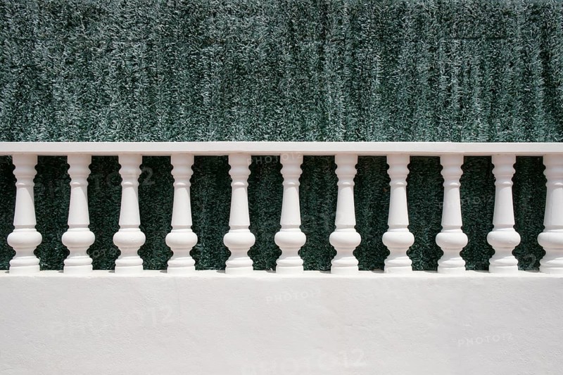 A white stone balustrade in front of an artificial green hedge