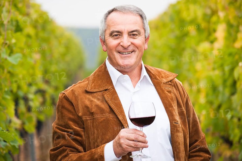 Winemaker or vintner standing with a glass of red wine in his vineyard