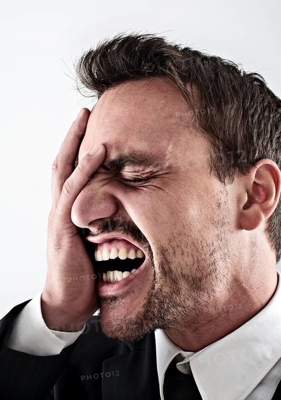 Desperate young man wearing a suit covering his face with his hand