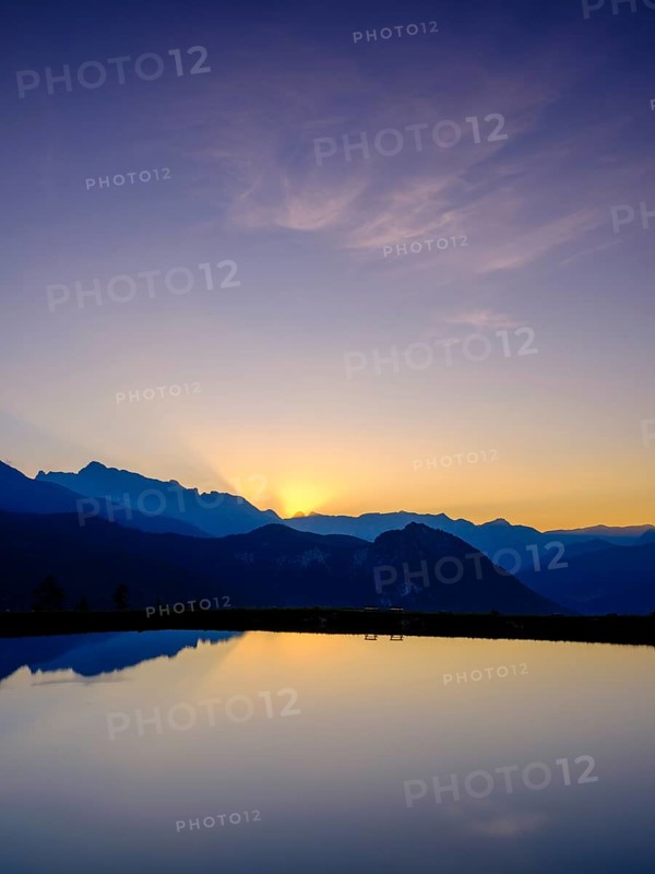 Mountain silhouettes are reflected in an artificial mountain lake at sunset