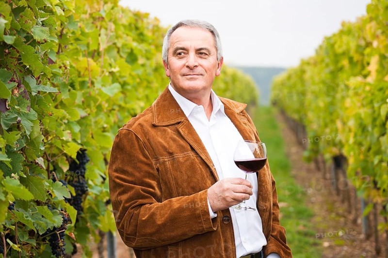 Winemaker or vintner standing with a glass of red wine in his vineyard