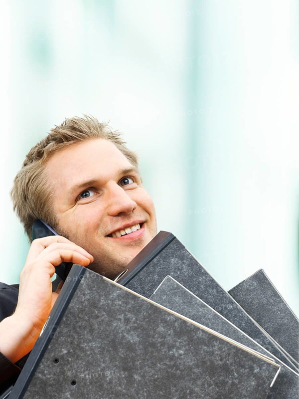 Businessman carrying ring binders while using a mobile phone