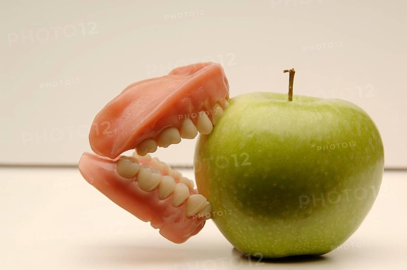 Dentures biting into a green apple