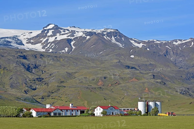 Farm located at the foot of a mountain in the middle of green meadows below the glaciated Eyjafjallajokull Volcano