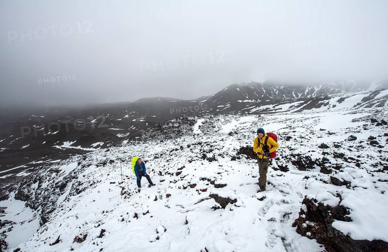 Hikers on hiking trail Tongariro Alpine Crossing in snow over lava fields