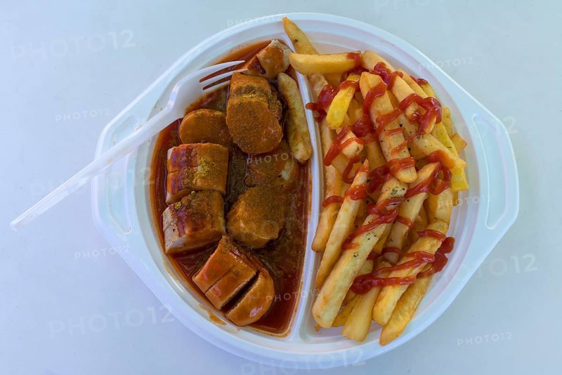 Currywurst with French fries with plastic fork on a plastic plate