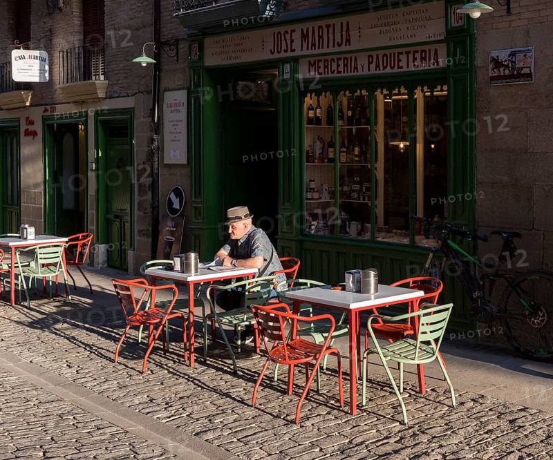 Old man reads newspapers and drinks coffee at a cafe table in early morning