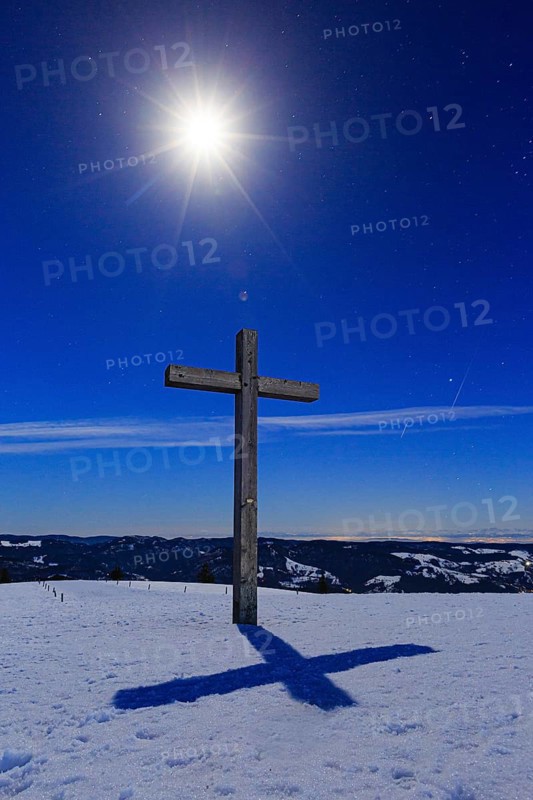 Summit cross in snow with starry sky by moonlight