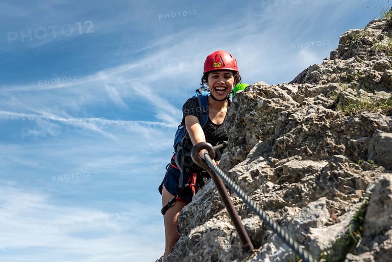 Laughing young woman with climbing helmet and on rock secured with rope