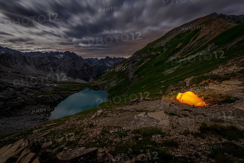 Tent in mountainous landscape with Lake Guffelsee in moonlight and cloudy sky