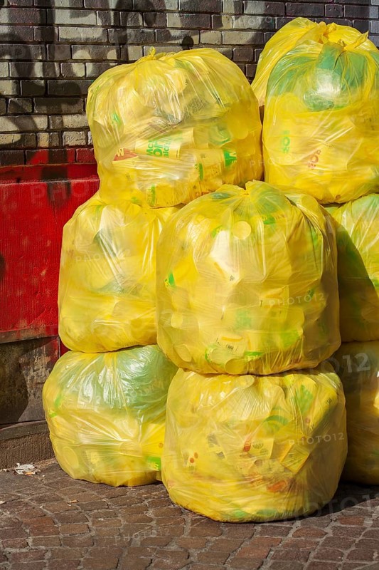 Stacked yellow bags for plastic waste in front of a house wall