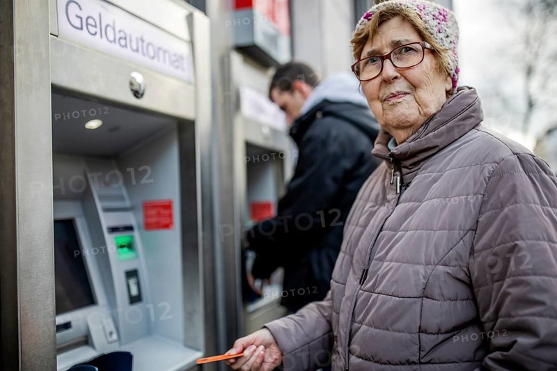 Senior citizen with cash card at ATM looks skeptical