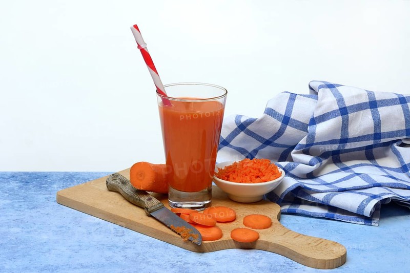 Carrot juice in glass and carrot slices on wooden board