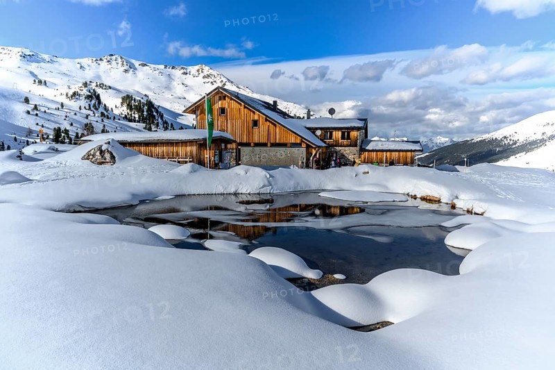 Snowy Lizumer Hut with small mountain lake in winter