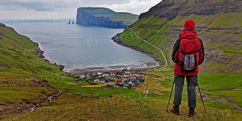 A hiker looks at the small village Tjornuvik and the Atlantic Ocean