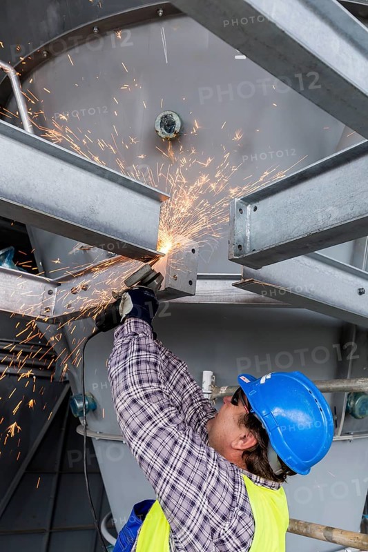 Construction worker processes a steel beam with an angle grinder on a large construction site