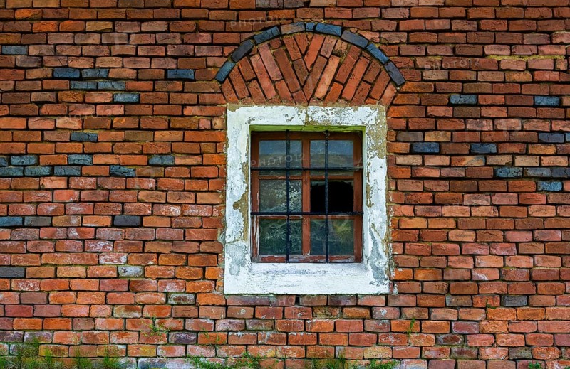 Wall of red bricks with barred stable window and broken panes