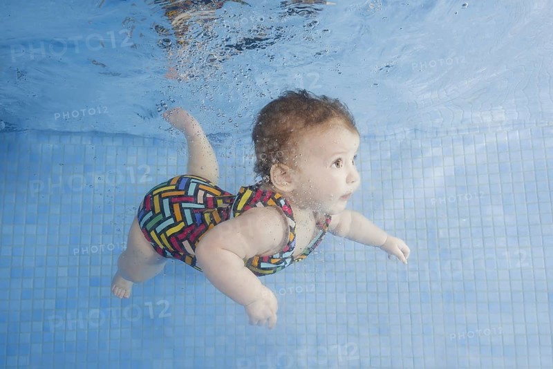 Little baby in a swimsuit learning to swim underwater in a swimming pool