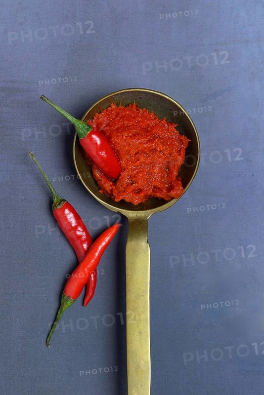 Red Thai curry paste in brass ladle and chilli peppers