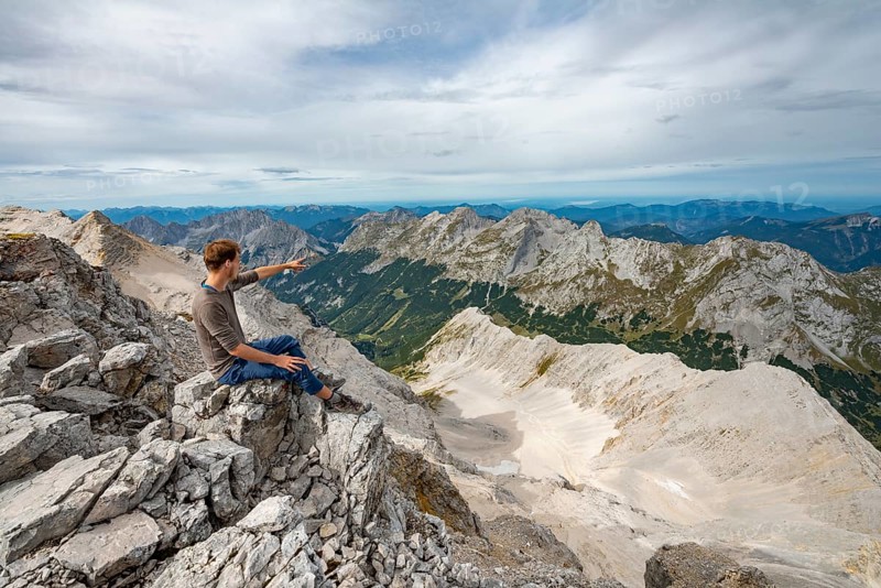 Hiker sitting at the summit of the Birkkarspitze pointing into the distance