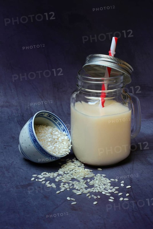 Rice milk in glass with drinking straw and rice grains