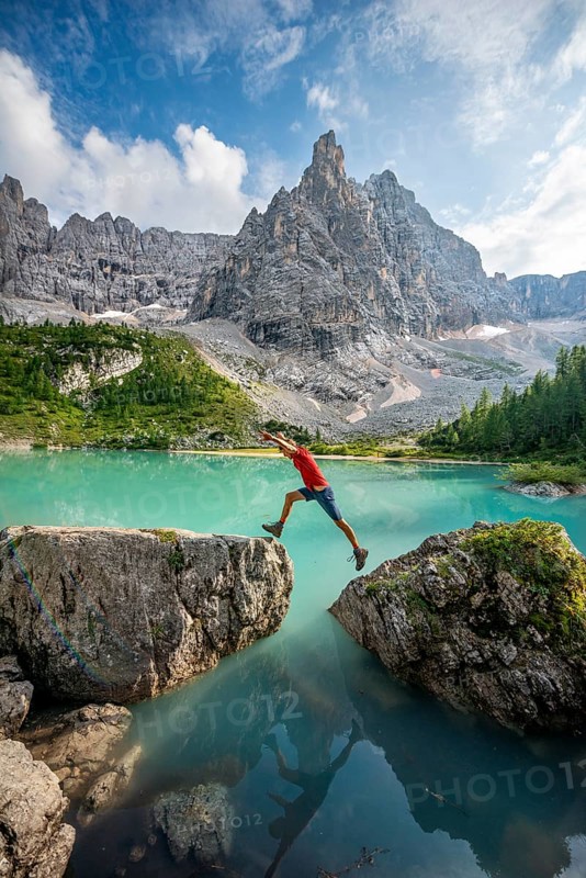 Hiker jumps from stone to stone at the turquoise green Sorapis lake