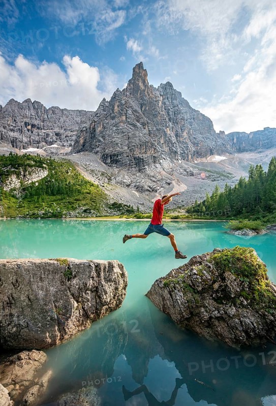 Hiker jumps from stone to stone at the turquoise green Sorapis lake