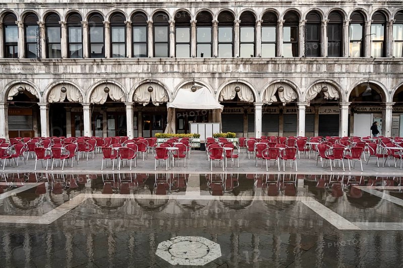 Red garden chairs in front of a coffee house near Acqua alta on St. Mark's Square