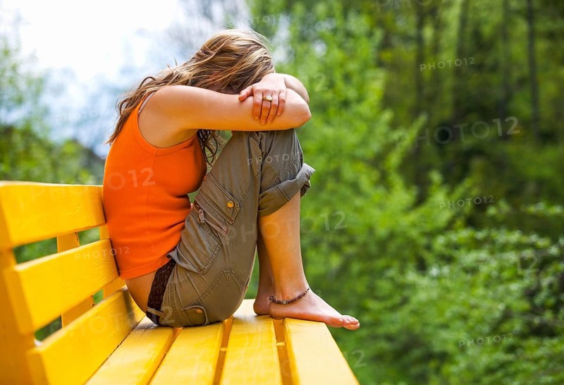 Young woman sitting sad and huddled on a bench