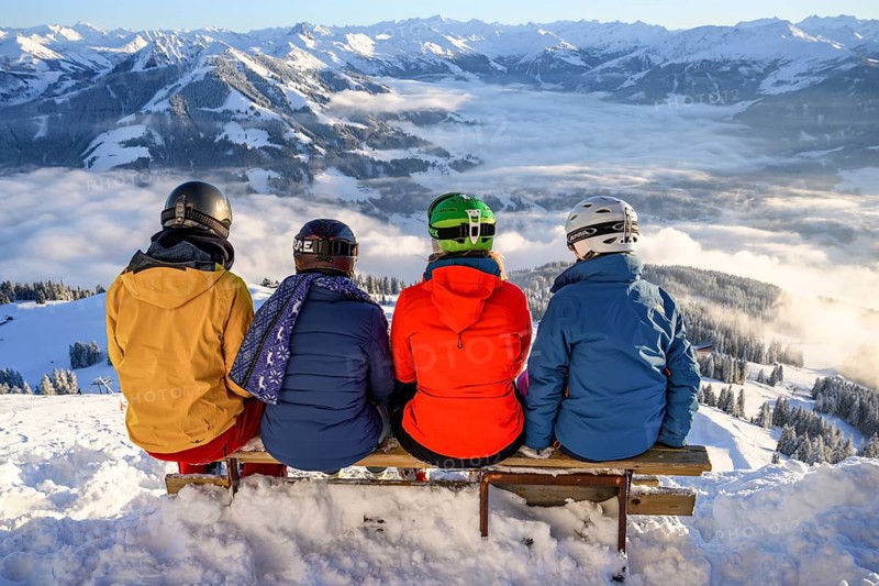 Skiers sitting on a bench and looking down on snow-covered mountains
