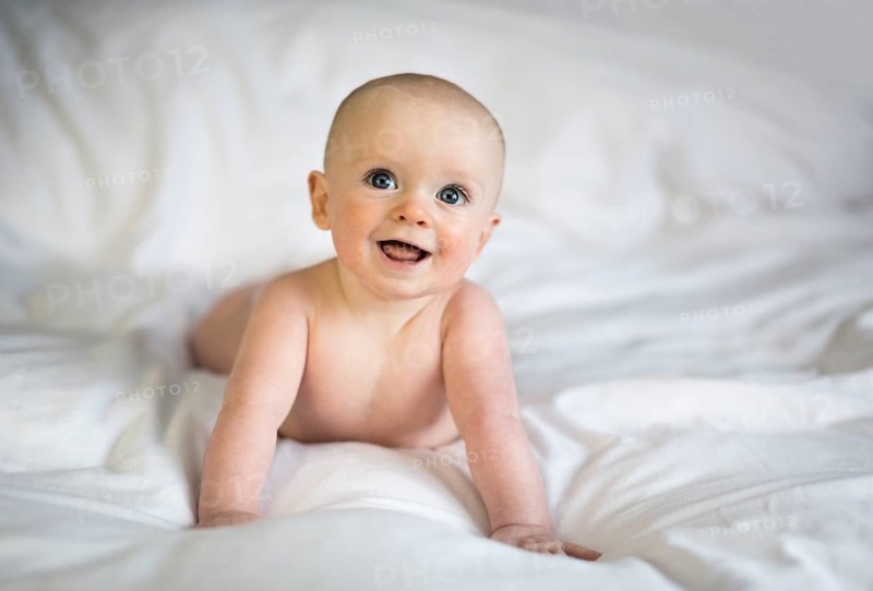 Baby boy on white bed sheets smiling