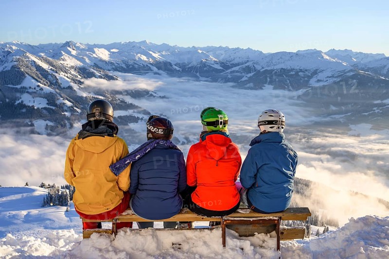 Skiers sitting on a bench and looking down on snow-covered mountains
