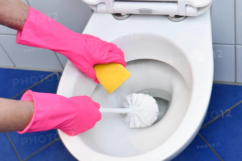 Person with rubber gloves cleans toilet with brush