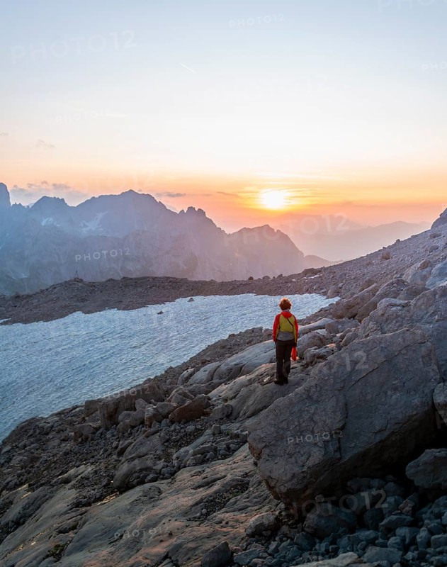 Hiker stands in rocky alpine terrain and looks at sunset over Gosaukamm with mountain peak Bischofsmuetze