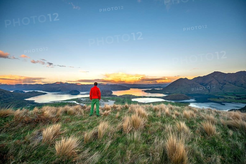 Walker looks out over Wanaka Lake and mountains at sunset, Rocky Peak