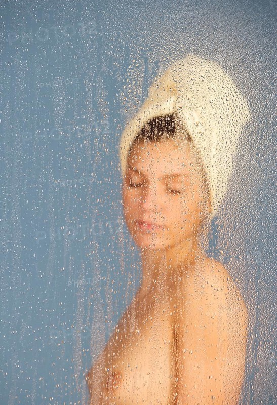 Woman sitting in a steam bath behind glass pane with drops of water, 24 years