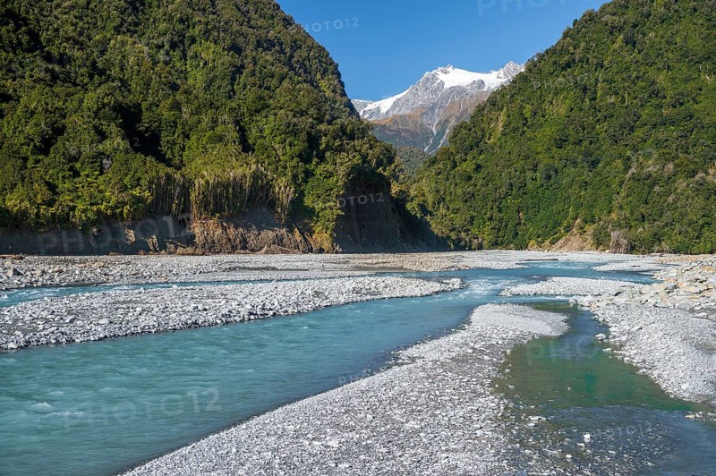 Gravel bed in the valley of the Karangarua River, forested slopes and glaciated peaks of New Zealand's Southern Alps