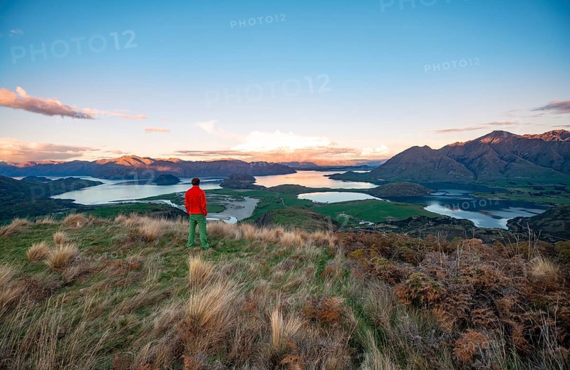 Walker looks out over Wanaka Lake and mountains at sunset, Rocky Peak