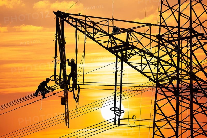 High voltage fitters working on the high voltage pylon at sunset, Baden-Wuerttemberg