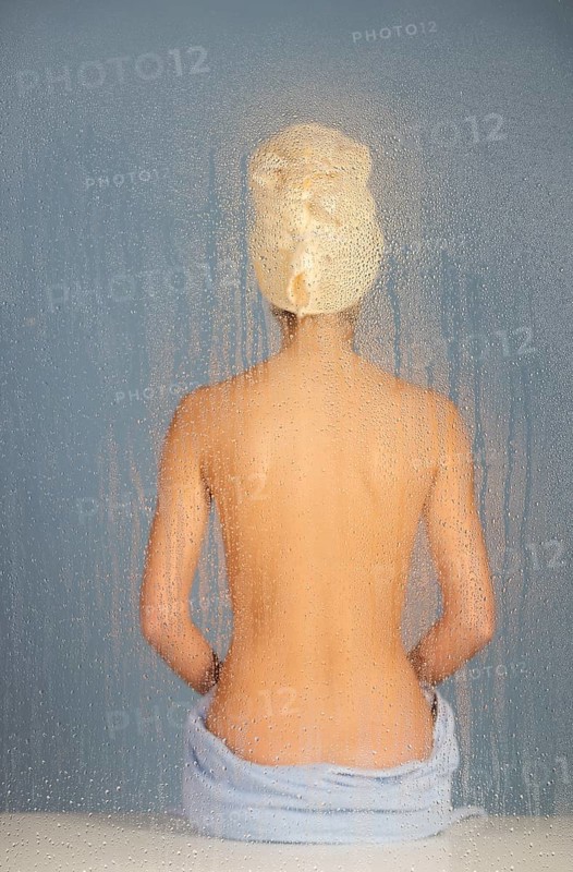 Woman sitting in a steam bath behind glass pane with drops of water, 24 years