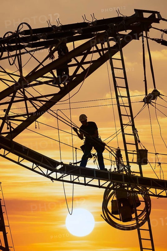 High voltage fitters working on the high voltage pylon at sunset, Baden-Wuerttemberg