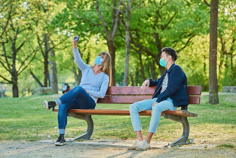 Man and woman wearing a face mask on a park bench in a municipal park
