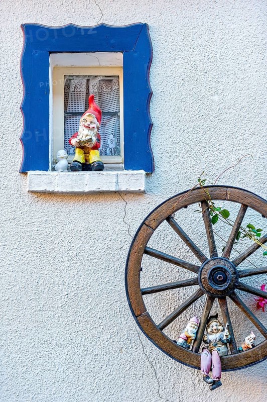 Garden gnomes at a small window and in a wooden wagon wheel