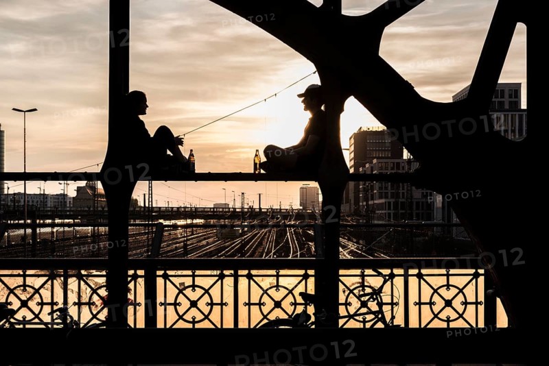 Two people sitting on the parapet and drinking against the light