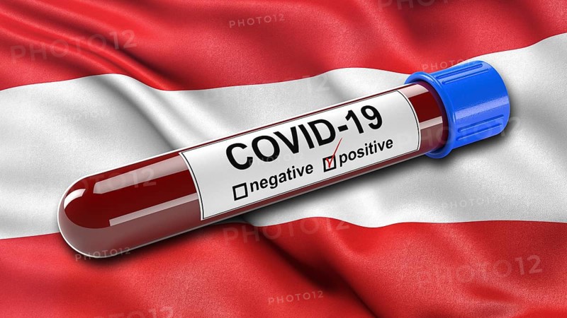 Flag of Austria waving in the wind with a positive Covid-19 blood tube