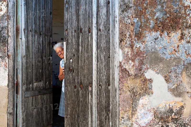 Woman at the entrance of her house with a decayed facade of crumbling plaster and a weathered wooden door