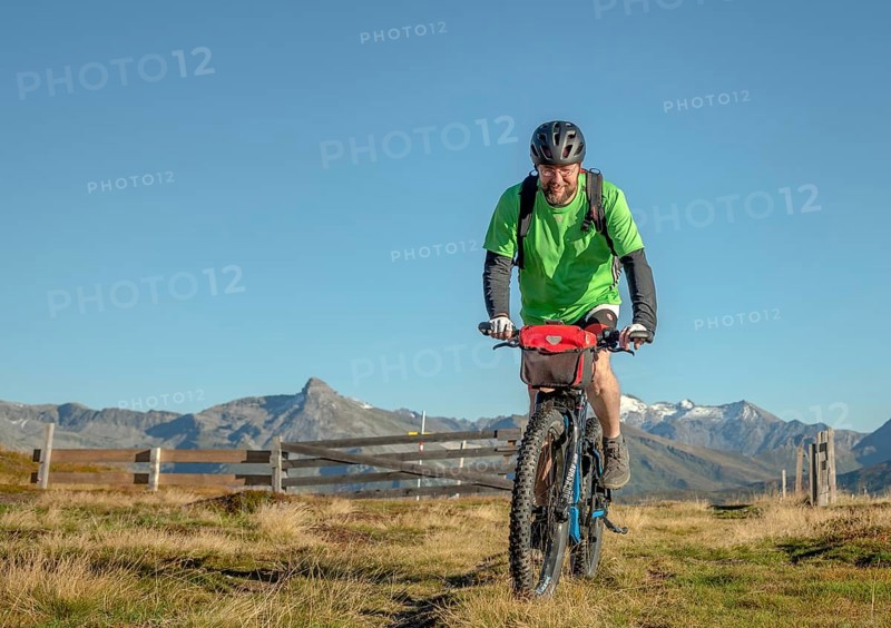 Mountain biker in his late forties rides on an ebike along an alpine path against a blue sky