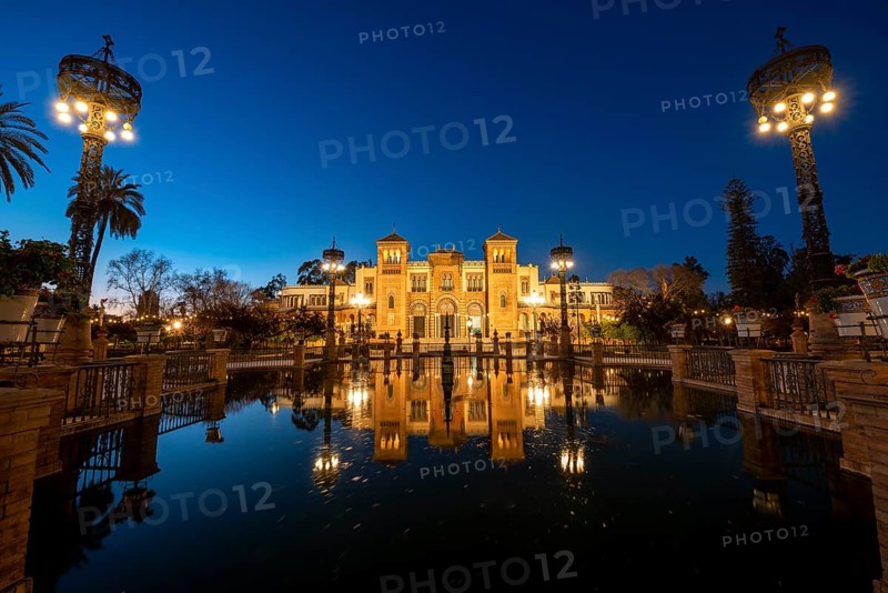 Illuminated art museum Museo de Artes y Costumbres Populares de Sevilla reflected in a fountain