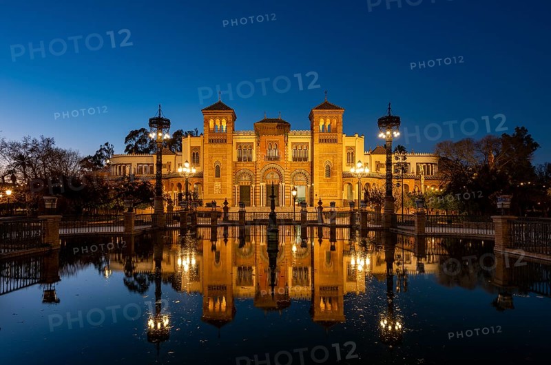 Illuminated art museum Museo de Artes y Costumbres Populares de Sevilla reflected in a fountain