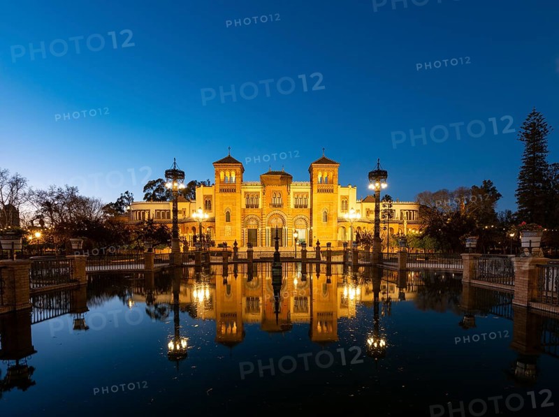 Illuminated art museum Museo de Artes y Costumbres Populares de Sevilla reflected in a fountain